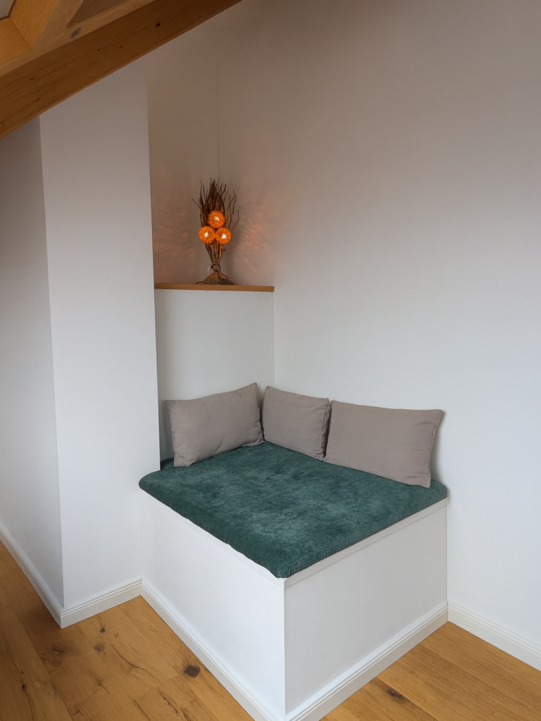 Nachher – Sitznische als neu geschaffener Raum Gemütliche Sitznische mit Holzverkleidung, Polstern und neu gewonnenem Wohnraum
